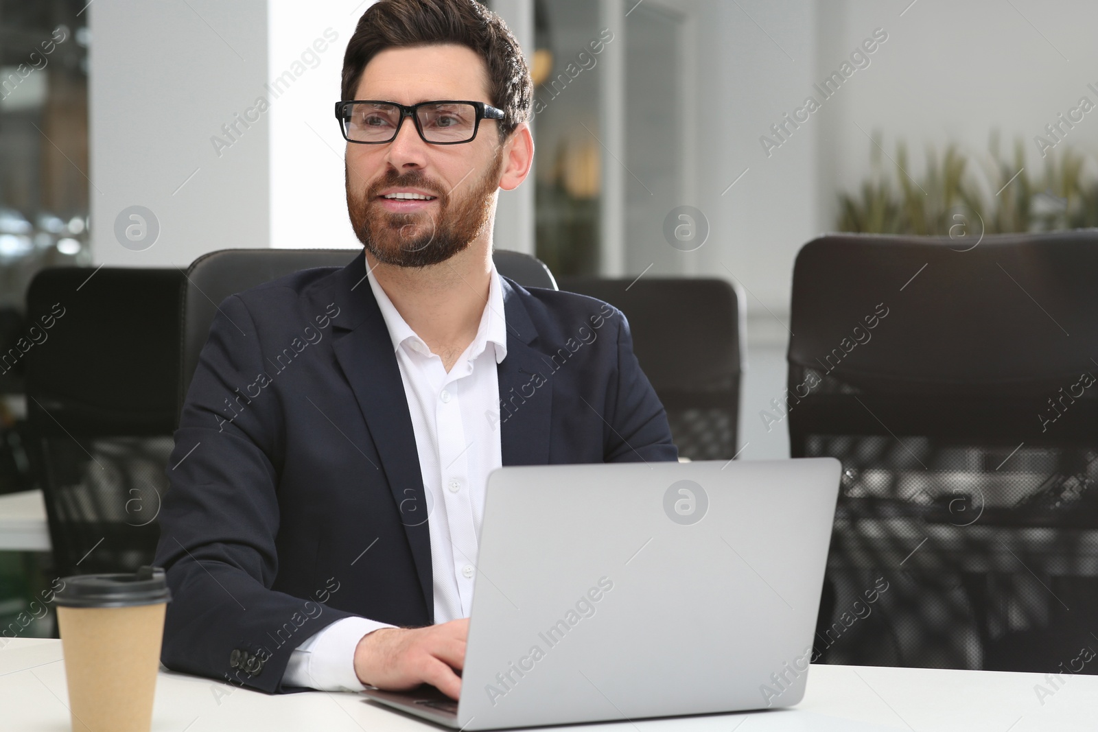 Photo of Man working on laptop at white desk in office