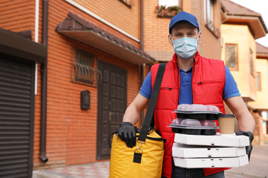 Photo of Courier in protective mask and gloves with orders near house outdoors. Food delivery service during coronavirus quarantine