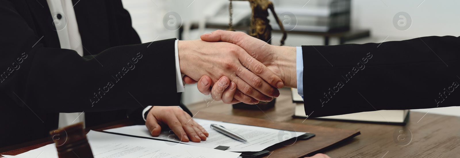 Image of Lawyer shaking hands with client at wooden table in office, closeup. Banner design