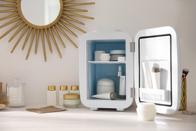 Photo of Cosmetics refrigerator and skin care products on white vanity table indoors