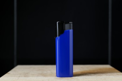 Photo of Blue plastic cigarette lighter on wooden table against black background, closeup