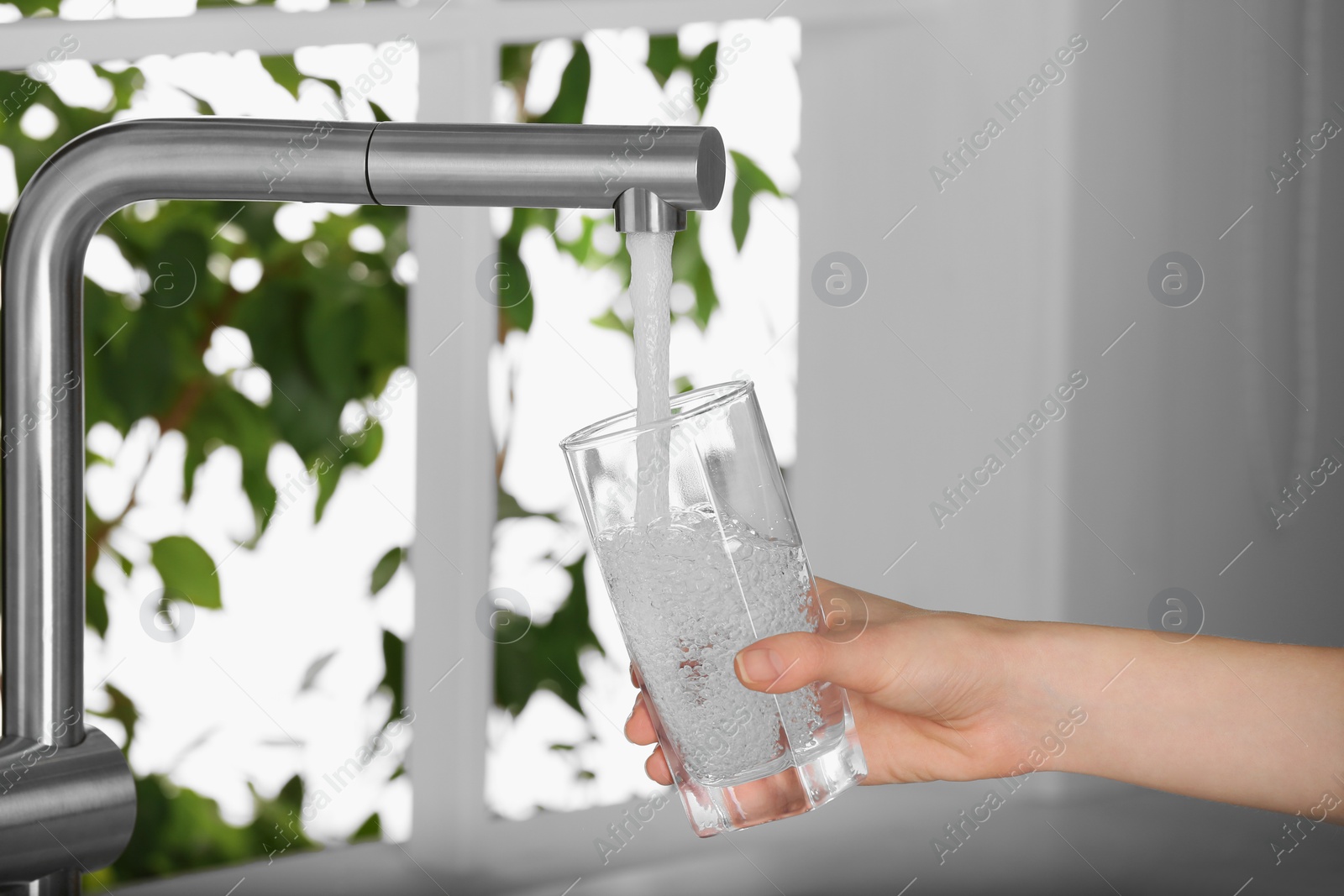 Photo of Woman filling glass with tap water from faucet in kitchen, closeup