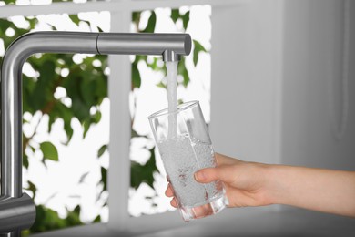 Photo of Woman filling glass with tap water from faucet in kitchen, closeup