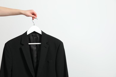 Photo of Woman holding hanger with black jacket near white wall, closeup. Space for text