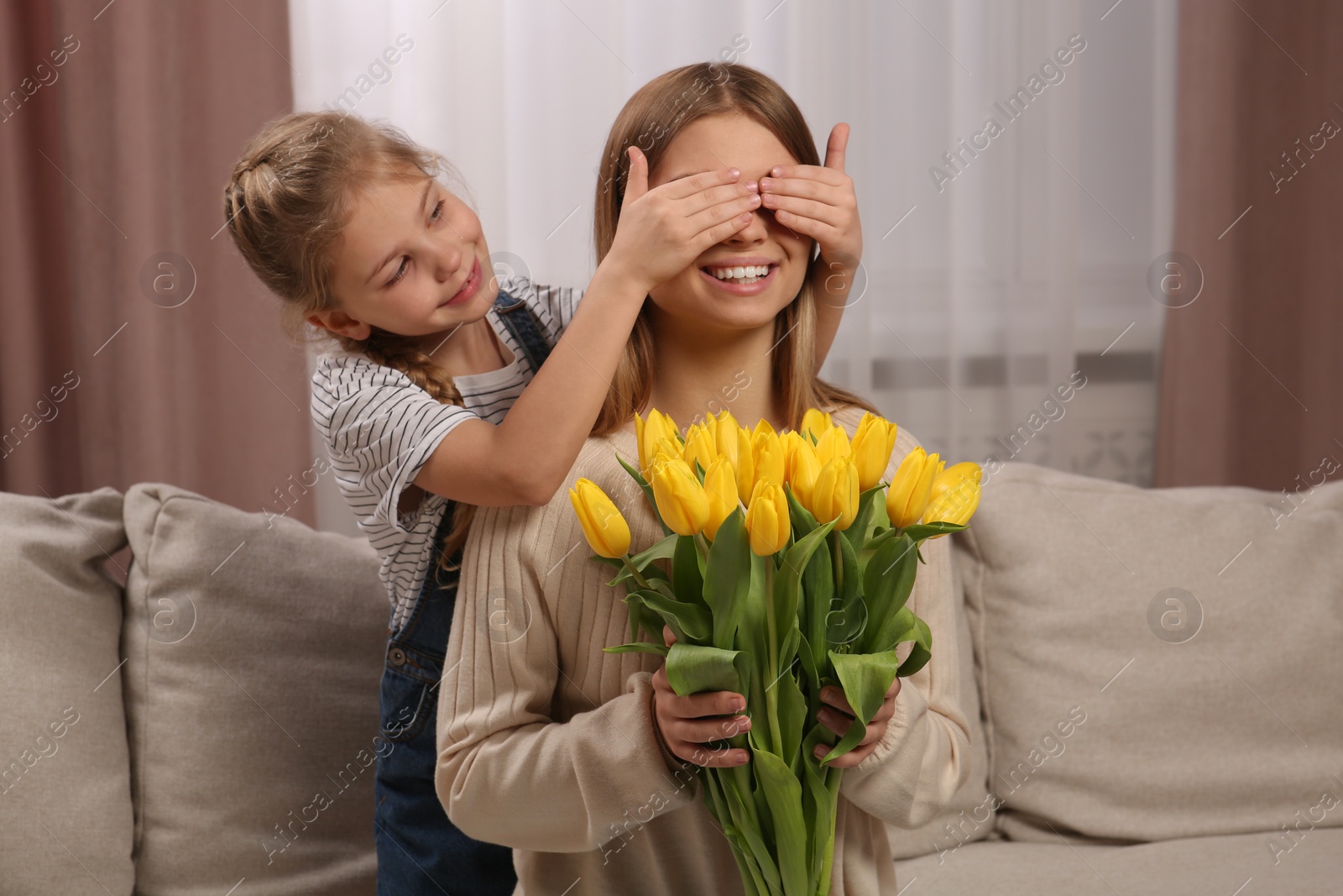 Photo of Little daughter congratulating mom with bouquet of yellow tulips at home. Happy Mother's Day