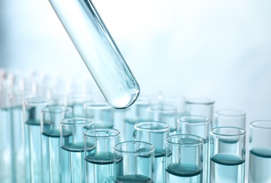 Photo of Taking test tube with liquid sample on light background, closeup