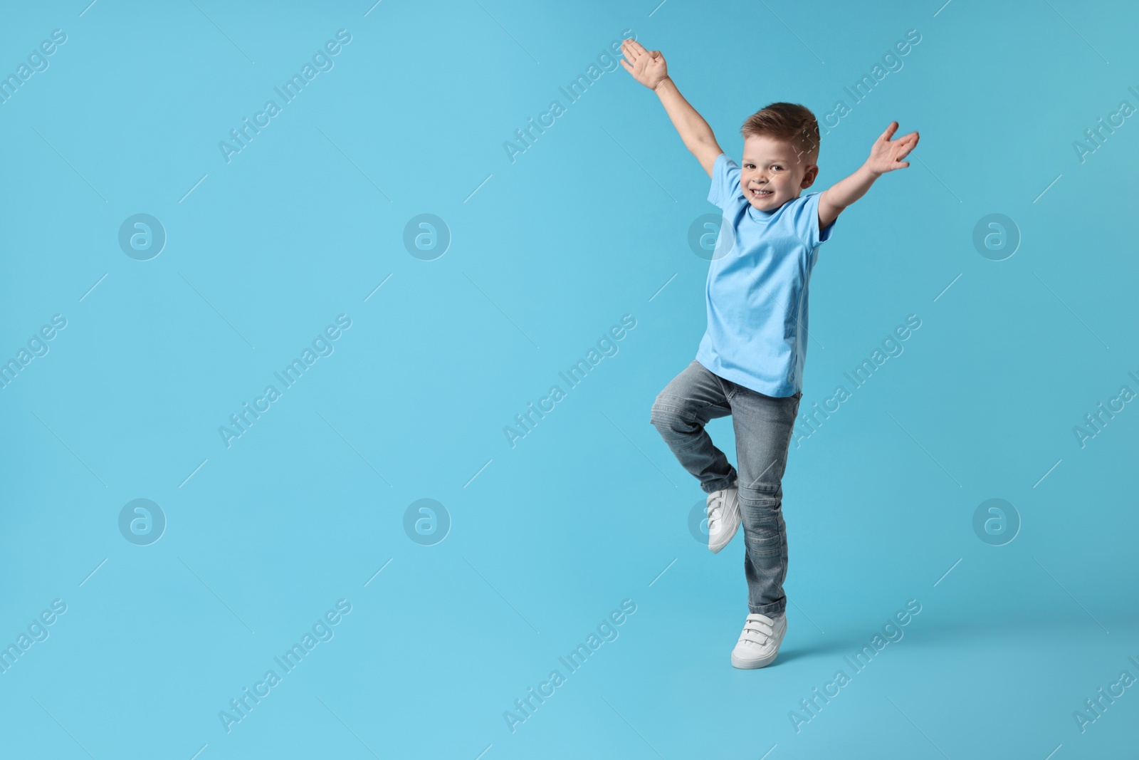 Photo of Happy little boy dancing on light blue background. Space for text