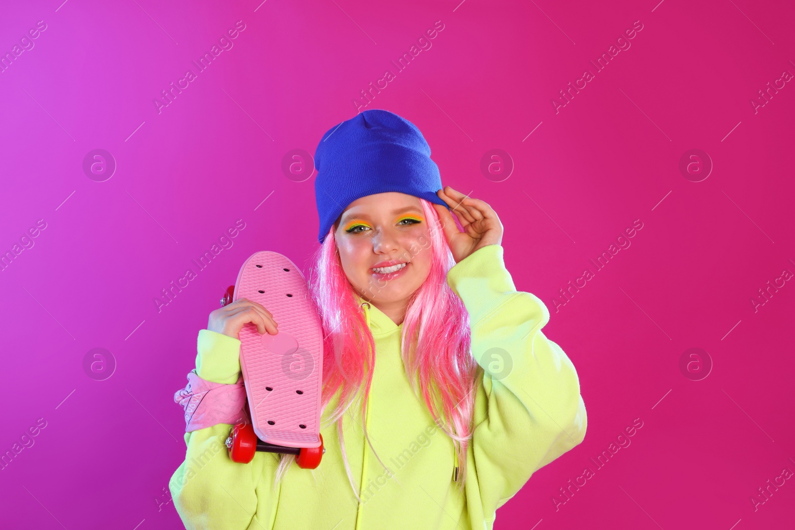 Photo of Cute indie girl with penny board on violet background