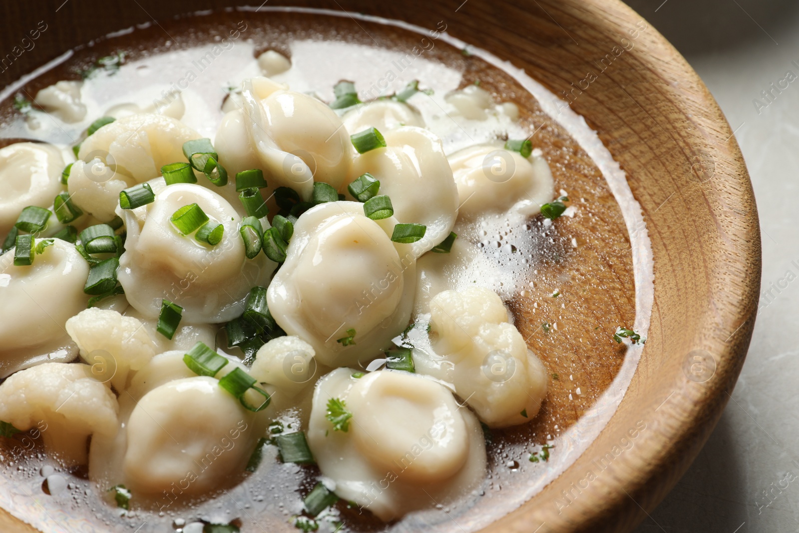 Photo of Plate of tasty dumplings with green onion in broth on table, closeup