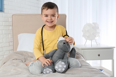 Photo of Cute child playing doctor with stuffed toy at hospital