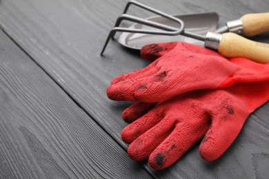 Gardening gloves, trowel and rake on grey wooden table, closeup. Space for text