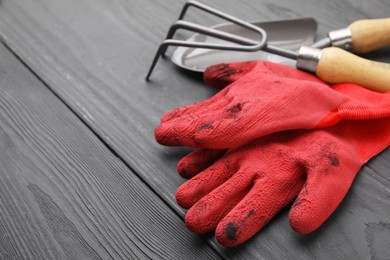 Photo of Gardening gloves, trowel and rake on grey wooden table, closeup. Space for text