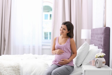 Photo of Happy pregnant woman sitting on bed at home