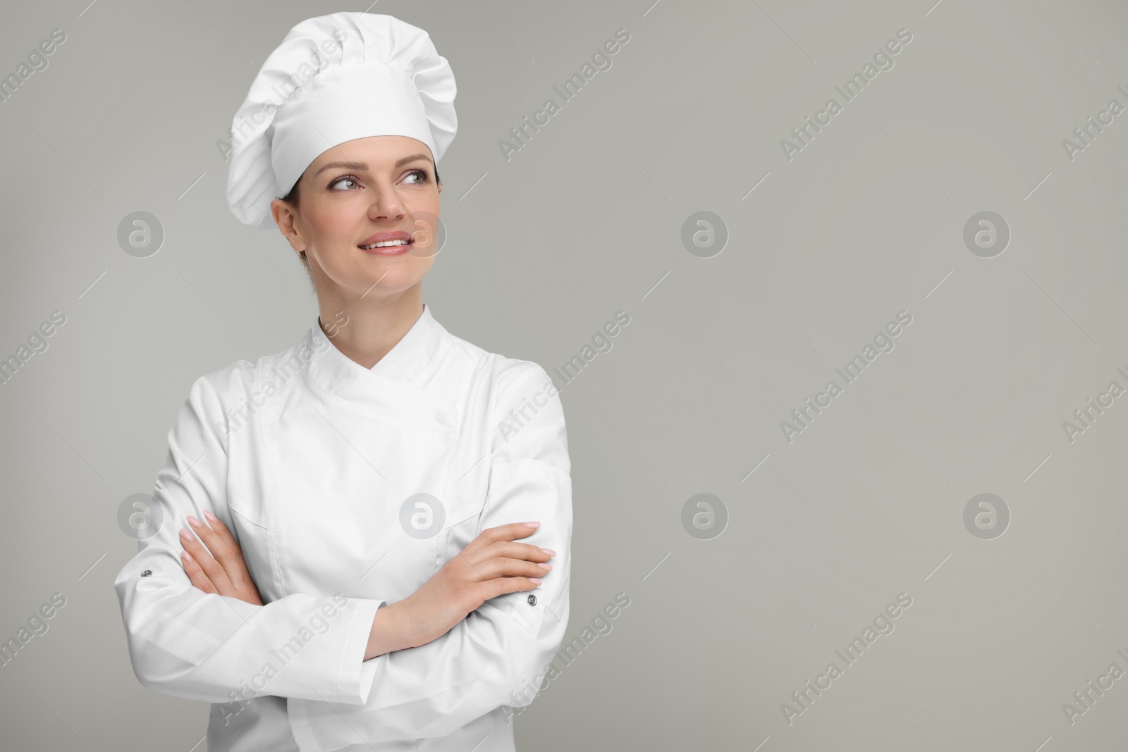 Photo of Happy woman chef in uniform on grey background, space for text