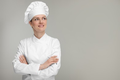 Happy woman chef in uniform on grey background, space for text