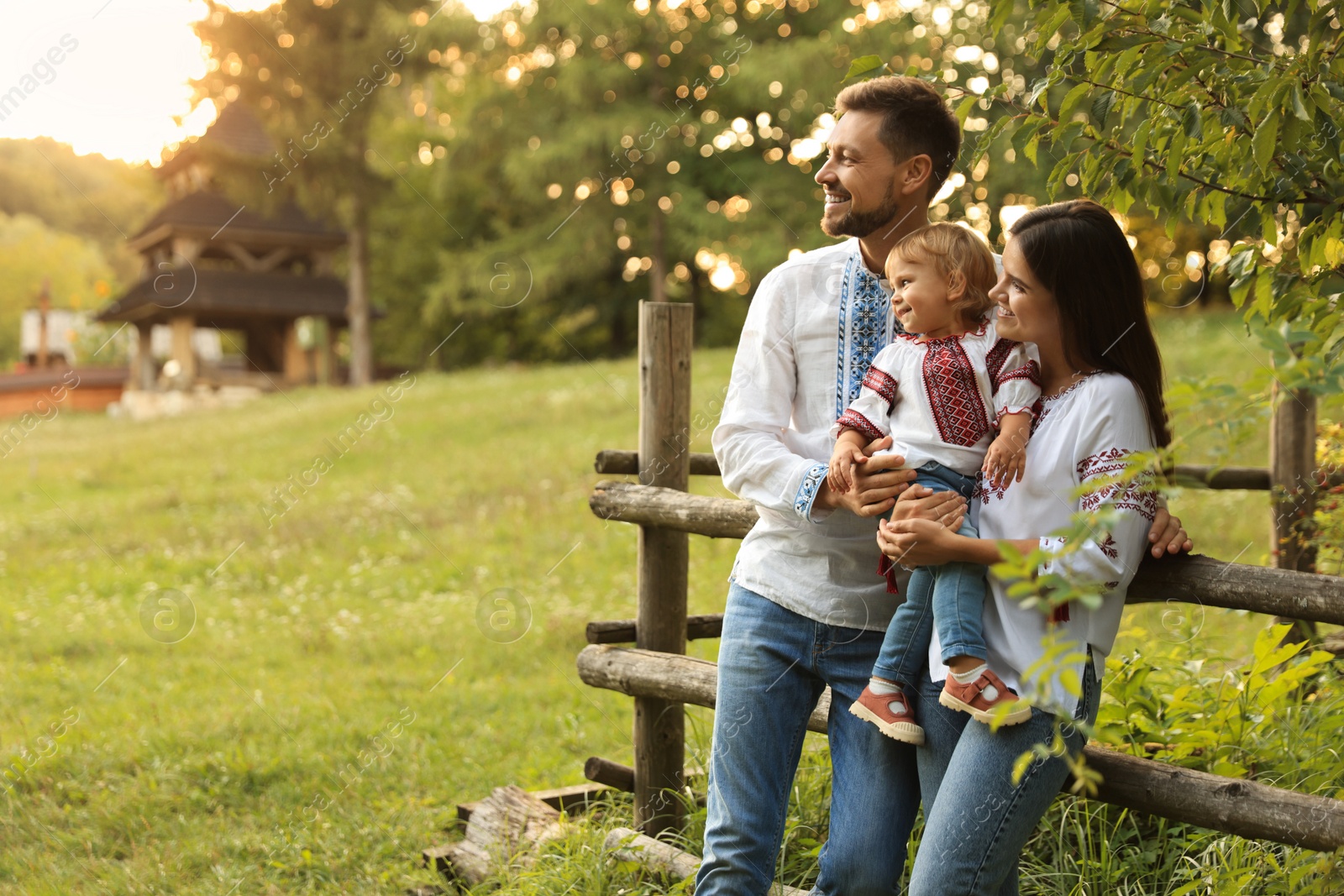 Photo of Happy cute family in embroidered Ukrainian shirts near rustic fence on sunny day. Space for text