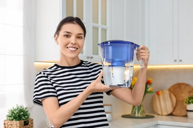 Woman holding filter jug with water in kitchen