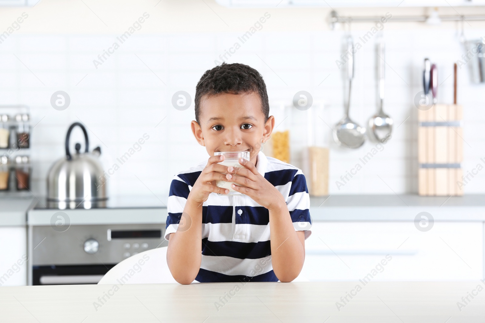 Photo of Adorable African-American boy with glass of milk in kitchen