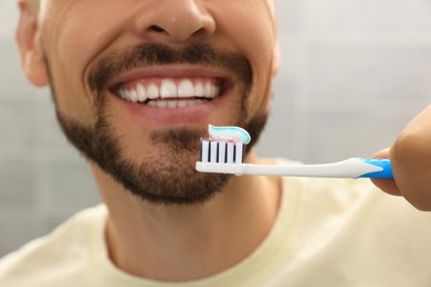 Photo of Man holding brush with toothpaste against blurred background, closeup
