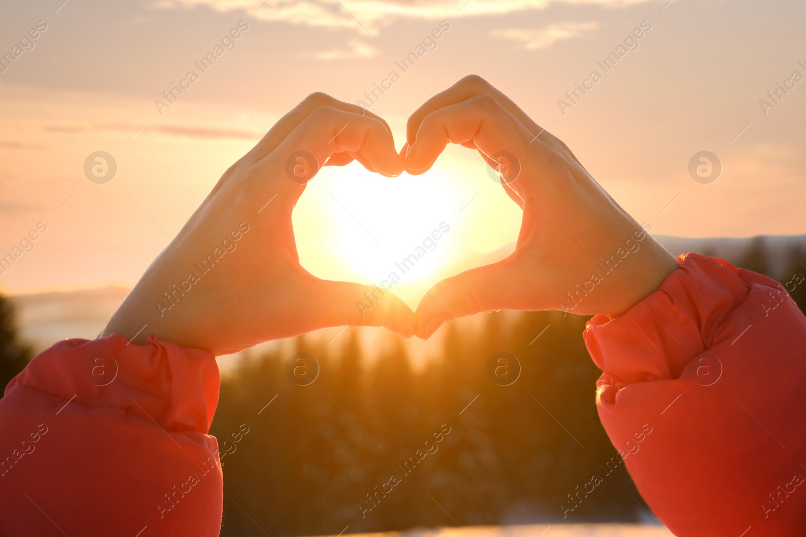 Photo of Woman making heart with hands outdoors at sunset, closeup. Winter vacation