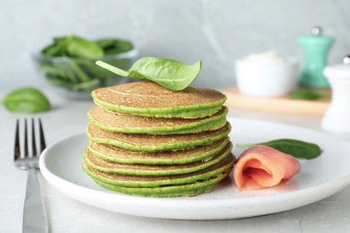 Tasty spinach pancakes with salmon on light grey table, closeup