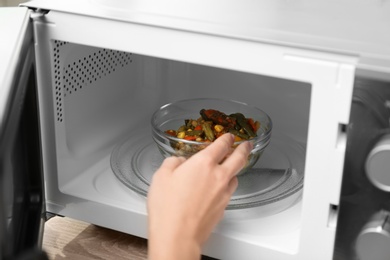 Photo of Young woman using microwave oven in kitchen, closeup