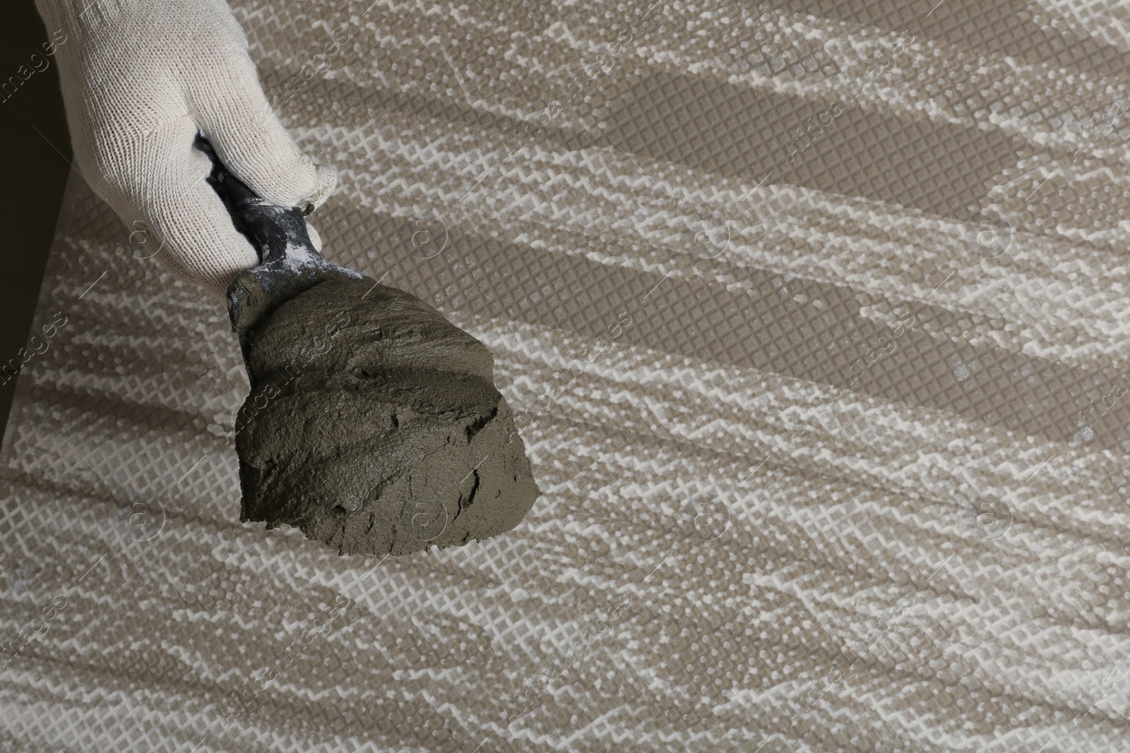 Photo of Worker holding adhesive mix on spatula above tile, closeup. Space for text