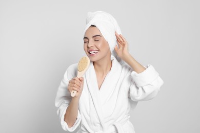 Woman in bathrobe with towel singing into brush on light grey background. Spa treatment