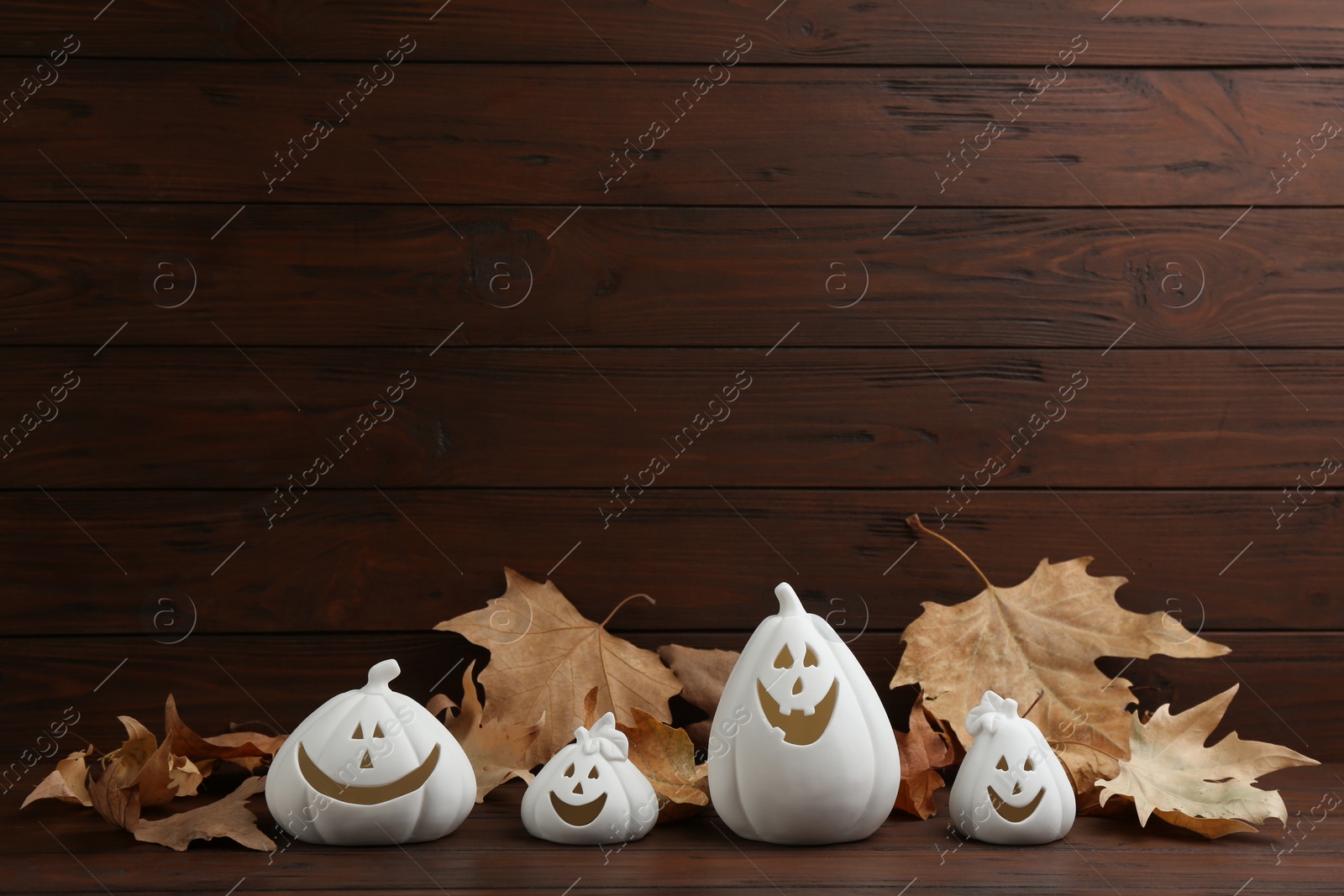 Image of White pumpkin shaped candle holders and dry leaves on wooden table. Halloween decoration