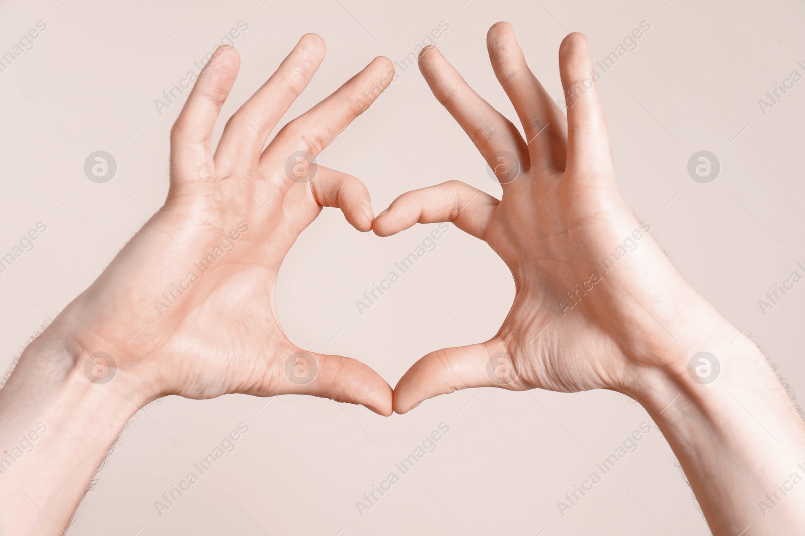 Photo of Young man making heart with his hands on light background, closeup