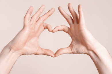 Photo of Young man making heart with his hands on light background, closeup