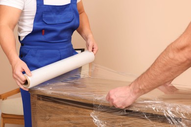 Photo of Workers wrapping chest of drawers in stretch film indoors, closeup