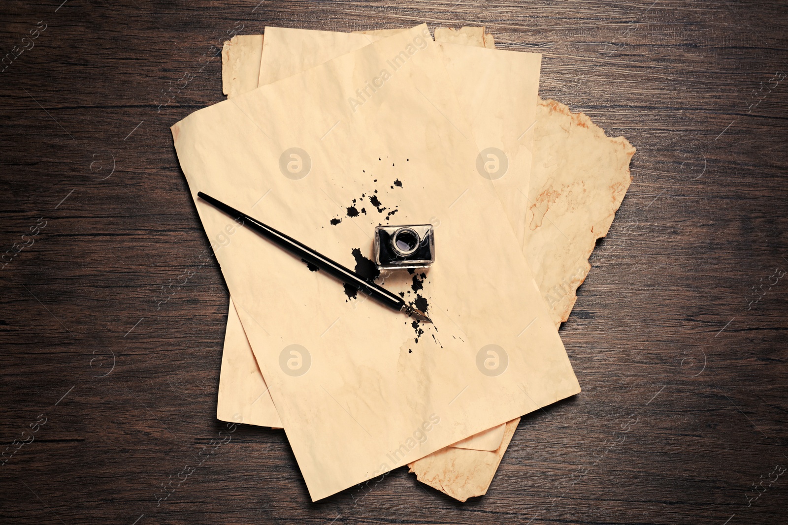 Photo of Inkwell, fountain pen and vintage parchment with ink stains on wooden table, top view