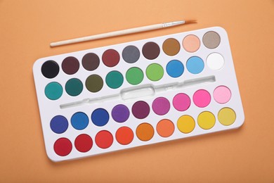 Photo of Watercolor palette and brush on pale orange background, flat lay