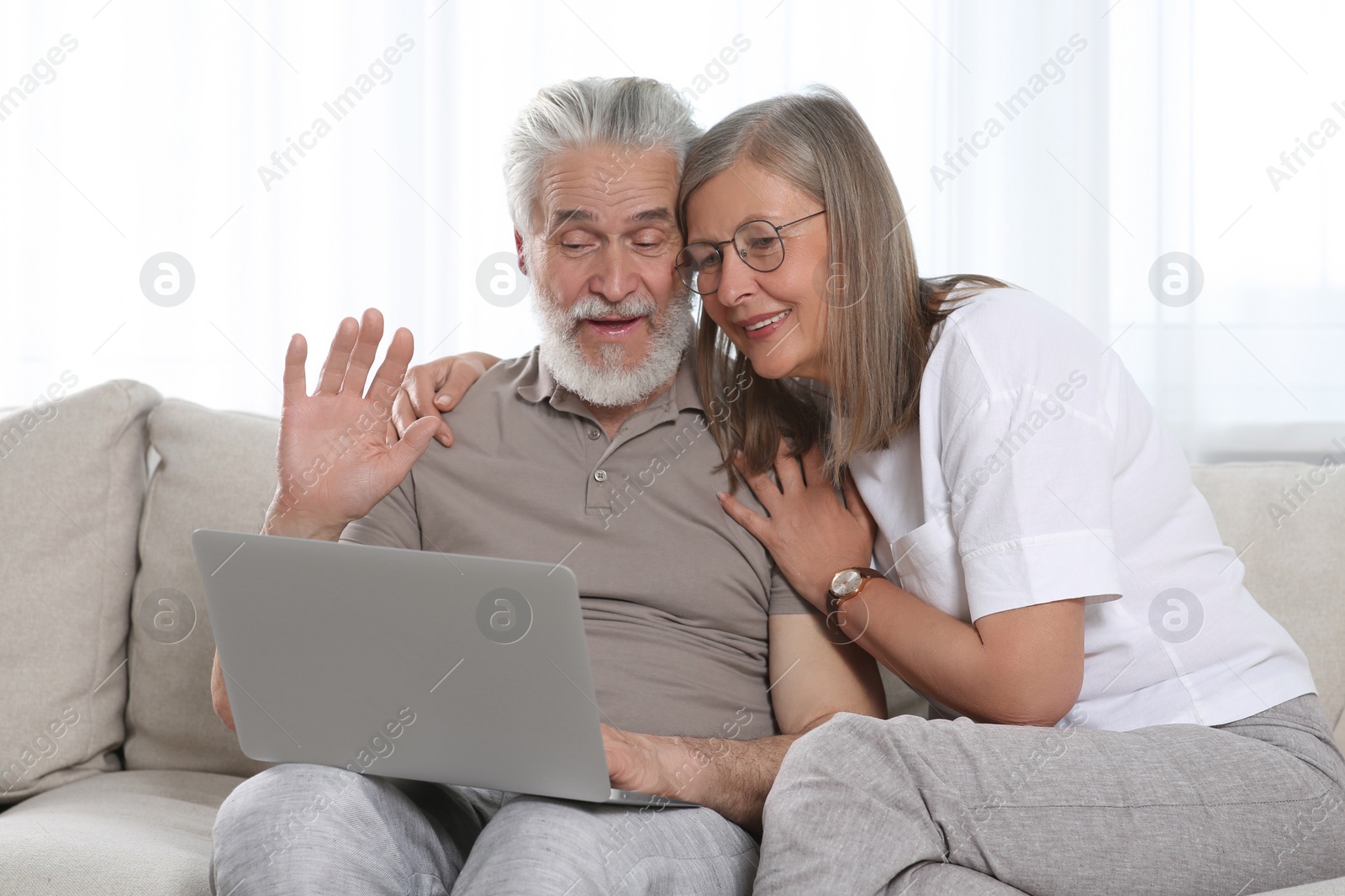 Photo of Senior couple using laptop on sofa at home