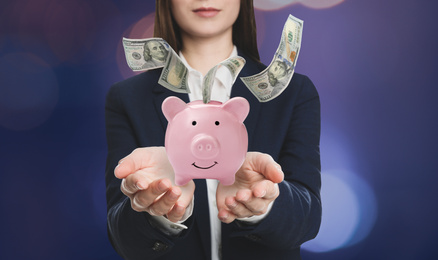 Young woman holding piggy bank and American dollars falling on color background, closeup 