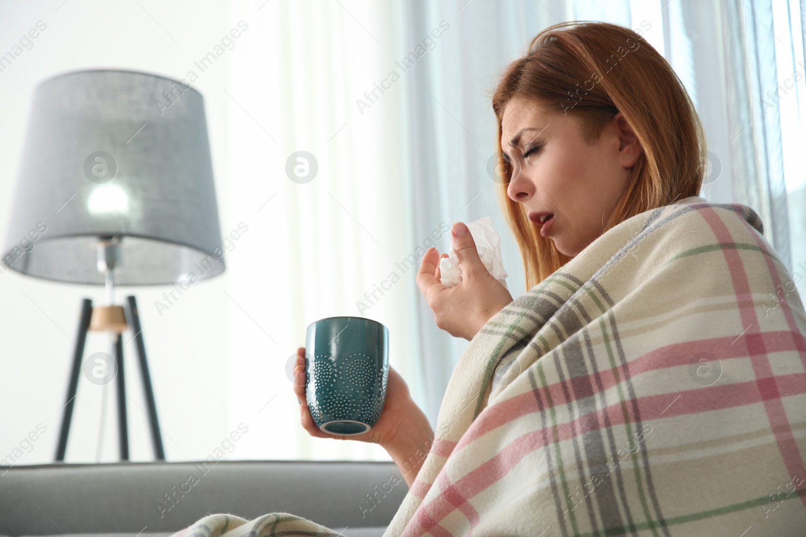 Photo of Sick woman wrapped in plaid with cup of hot drink at home. Influenza virus