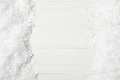 Frame made of snow on white wooden background, top view with space for text. Christmas season
