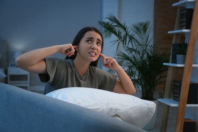 Unhappy young woman covering ears in living room at night. Noisy neighbours