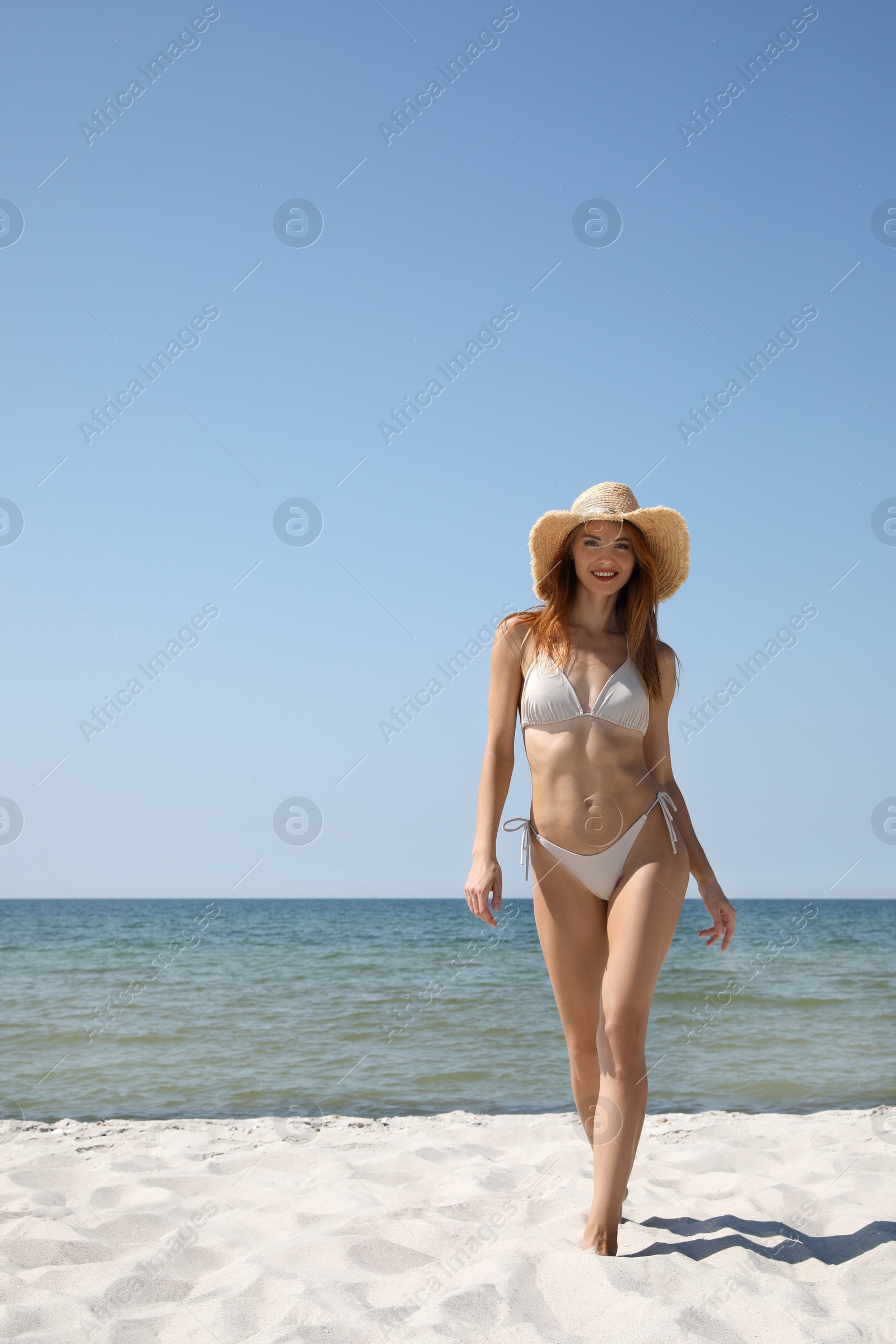 Photo of Attractive woman in bikini walking on sandy beach near sea