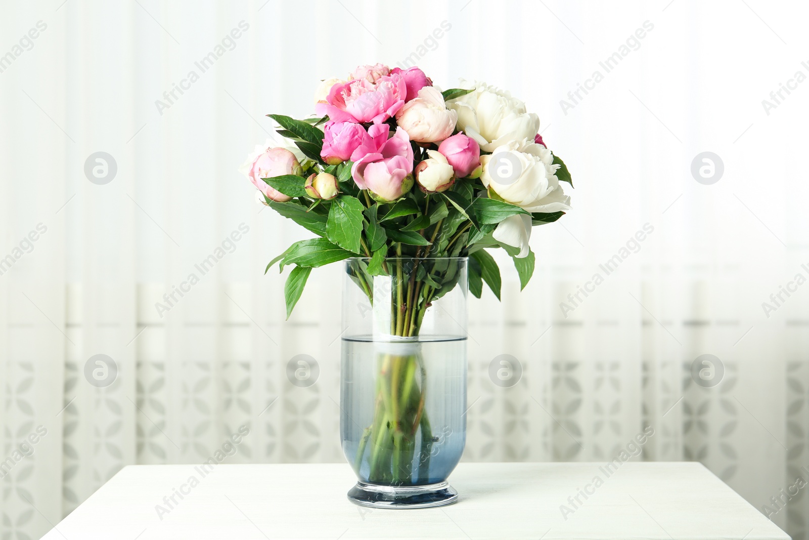 Photo of Bouquet of beautiful peonies in vase on white table