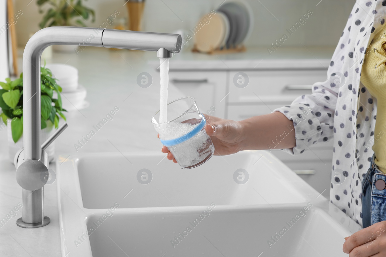 Photo of Woman filling glass with water from tap in kitchen, closeup