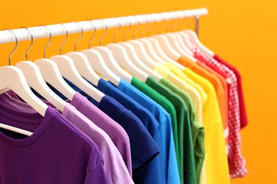 Rack with rainbow clothes on color background