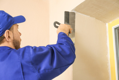 Professional worker plastering window area with putty knife indoors, closeup. Interior repair