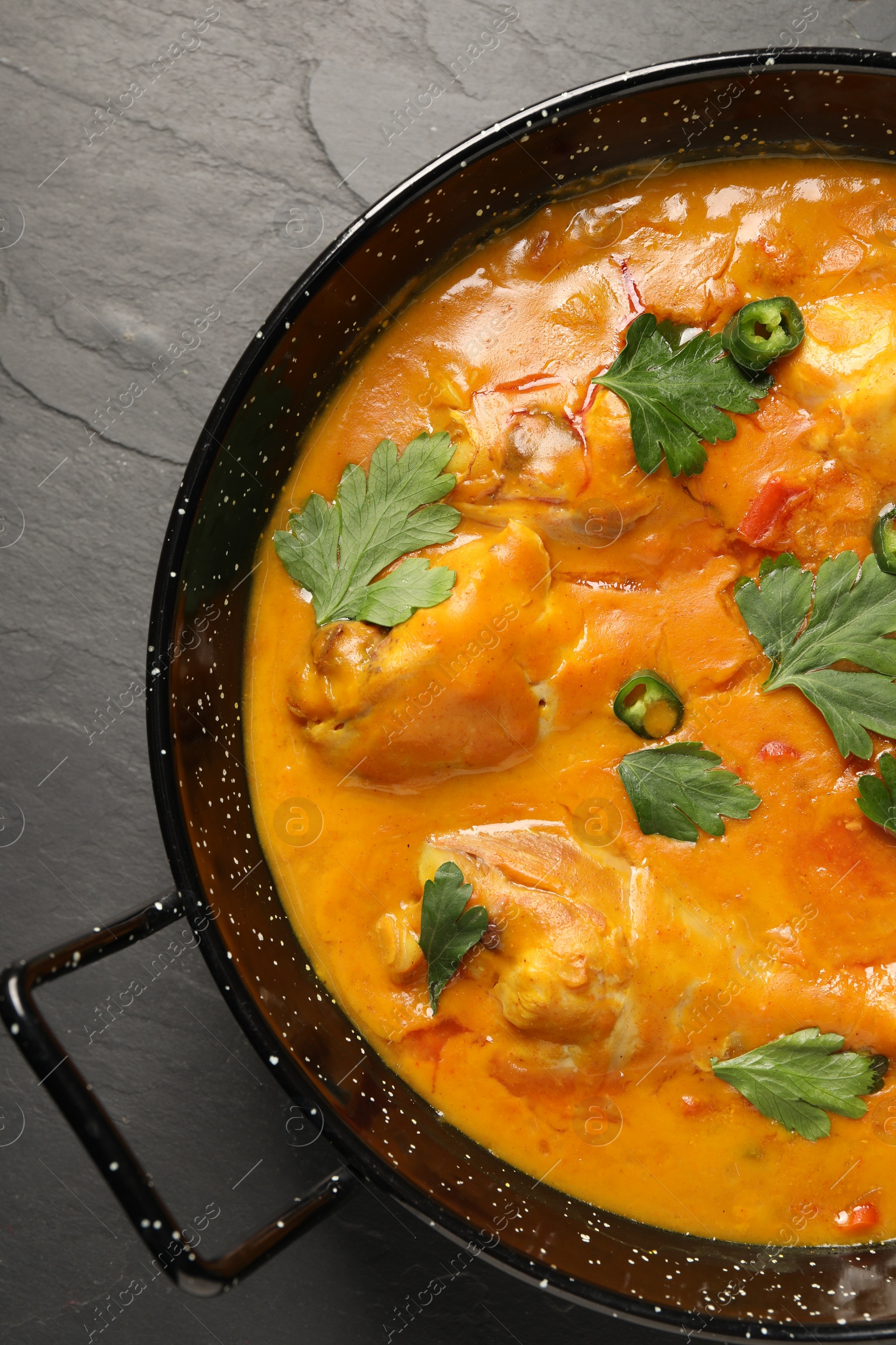 Photo of Tasty chicken curry with parsley and pepper on black textured table, top view