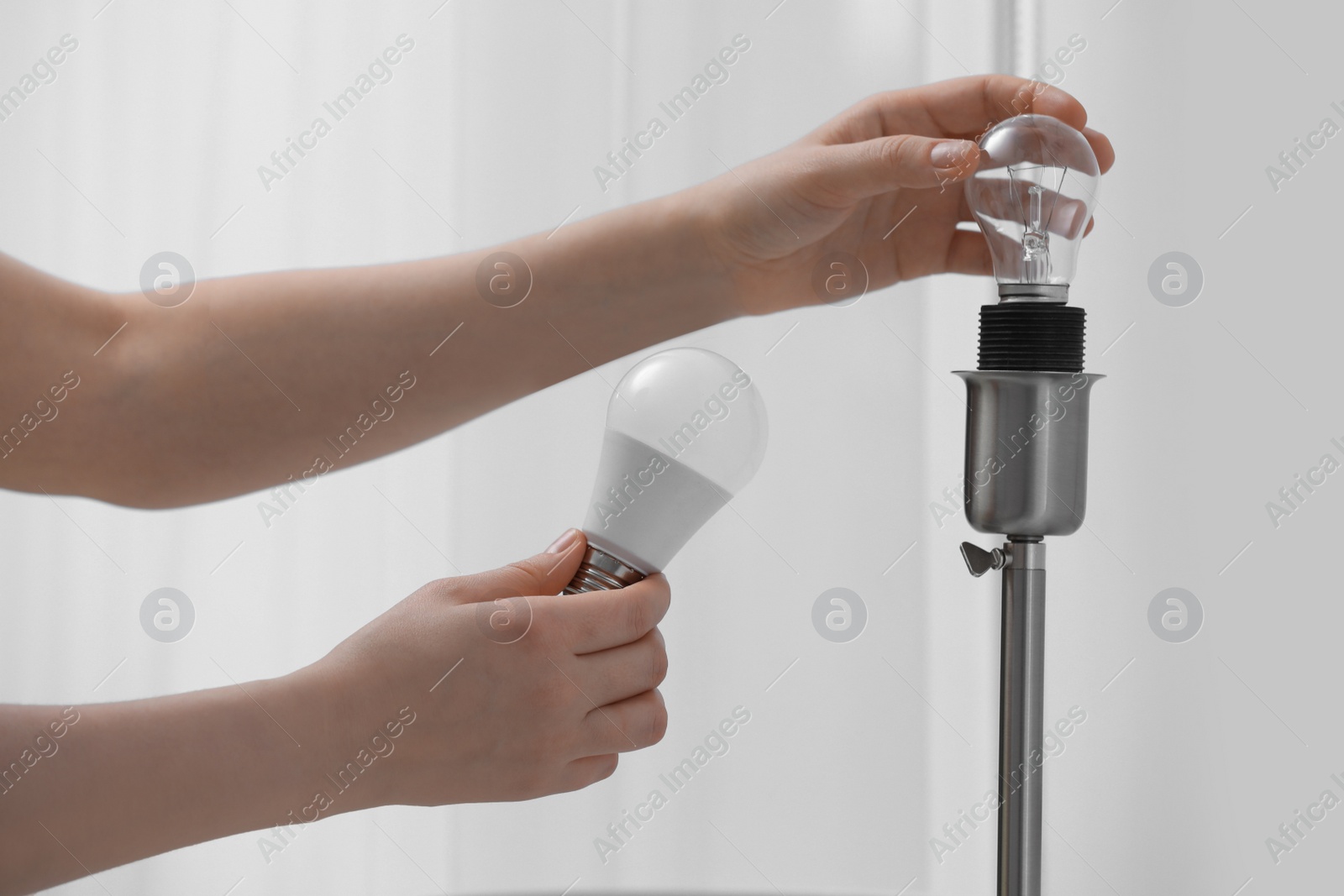 Photo of Woman changing incandescent light bulb for fluorescent one in lamp at home, closeup. Saving energy concept