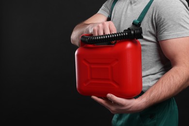 Man holding red canister on black background, closeup. Space for text