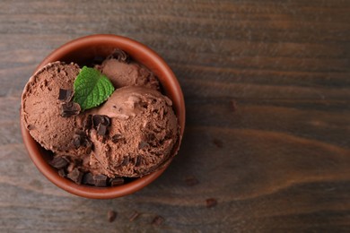 Photo of Bowl of tasty ice cream with chocolate chunks and mint on wooden table, top view. Space for text