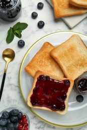 Photo of Delicious toasts served with jam, mint and berries on white marble table, flat lay