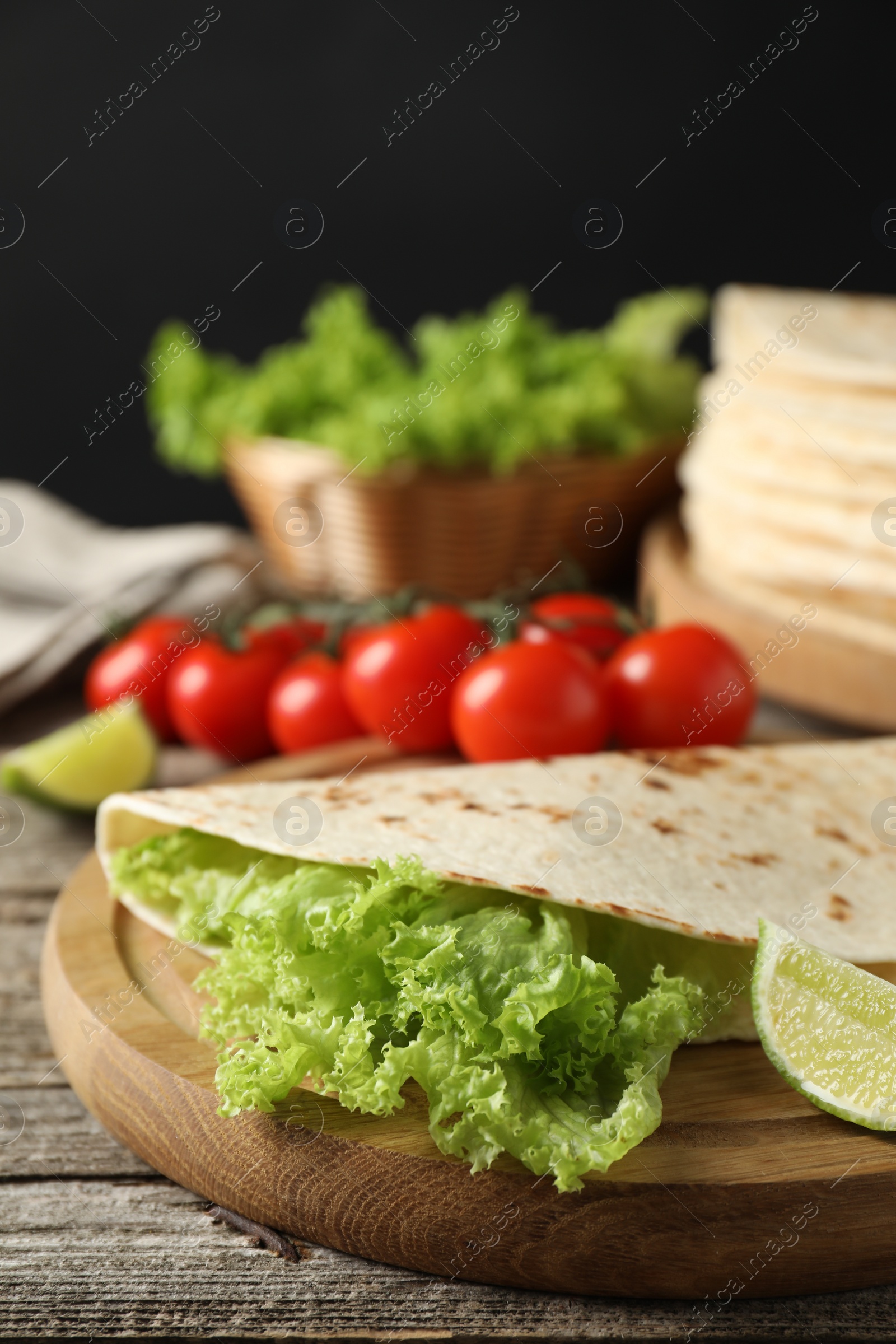 Photo of Tasty homemade tortilla, lettuce, lime and tomatoes on wooden table